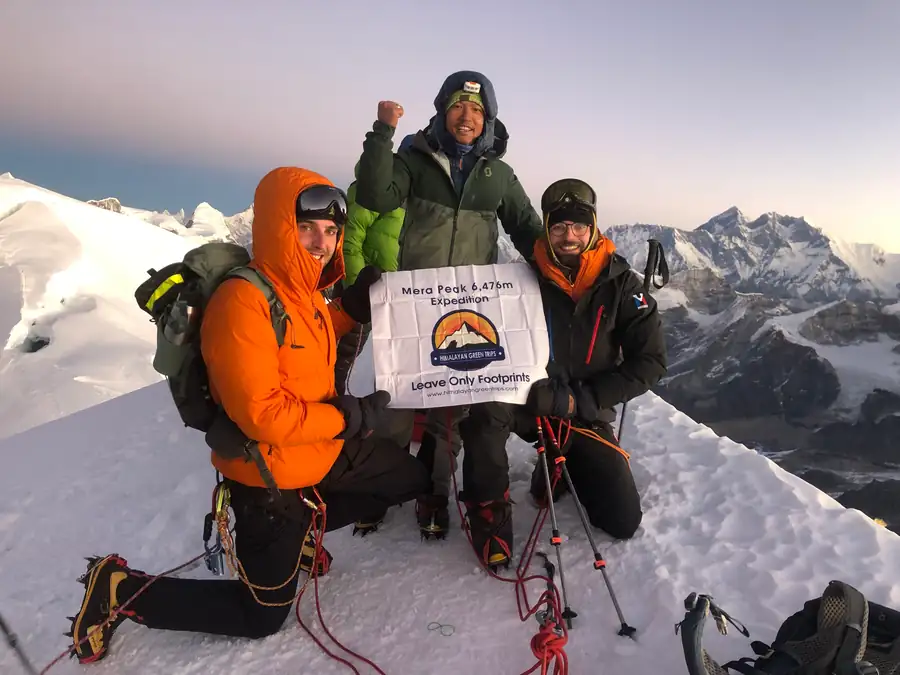 A Himalayan Green Trips team on the summit of Mera Peak, holding a banner that reads Mera Peak 6,476m Expedition
