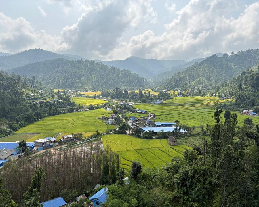Terraced fields and village buildings among forested hills beneath a cloudy sky